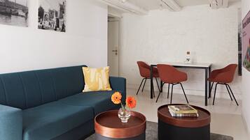 A modern living room with a teal sofa, a coffee table with a vase of flowers, and a dining area with a table and chairs.