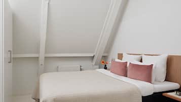 A bedroom with a bed, a nightstand, a radiator, and a window.