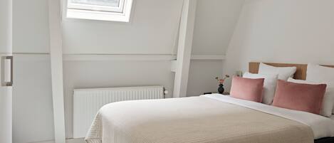 A bedroom with a bed, a window, a radiator, and a nightstand with a vase.