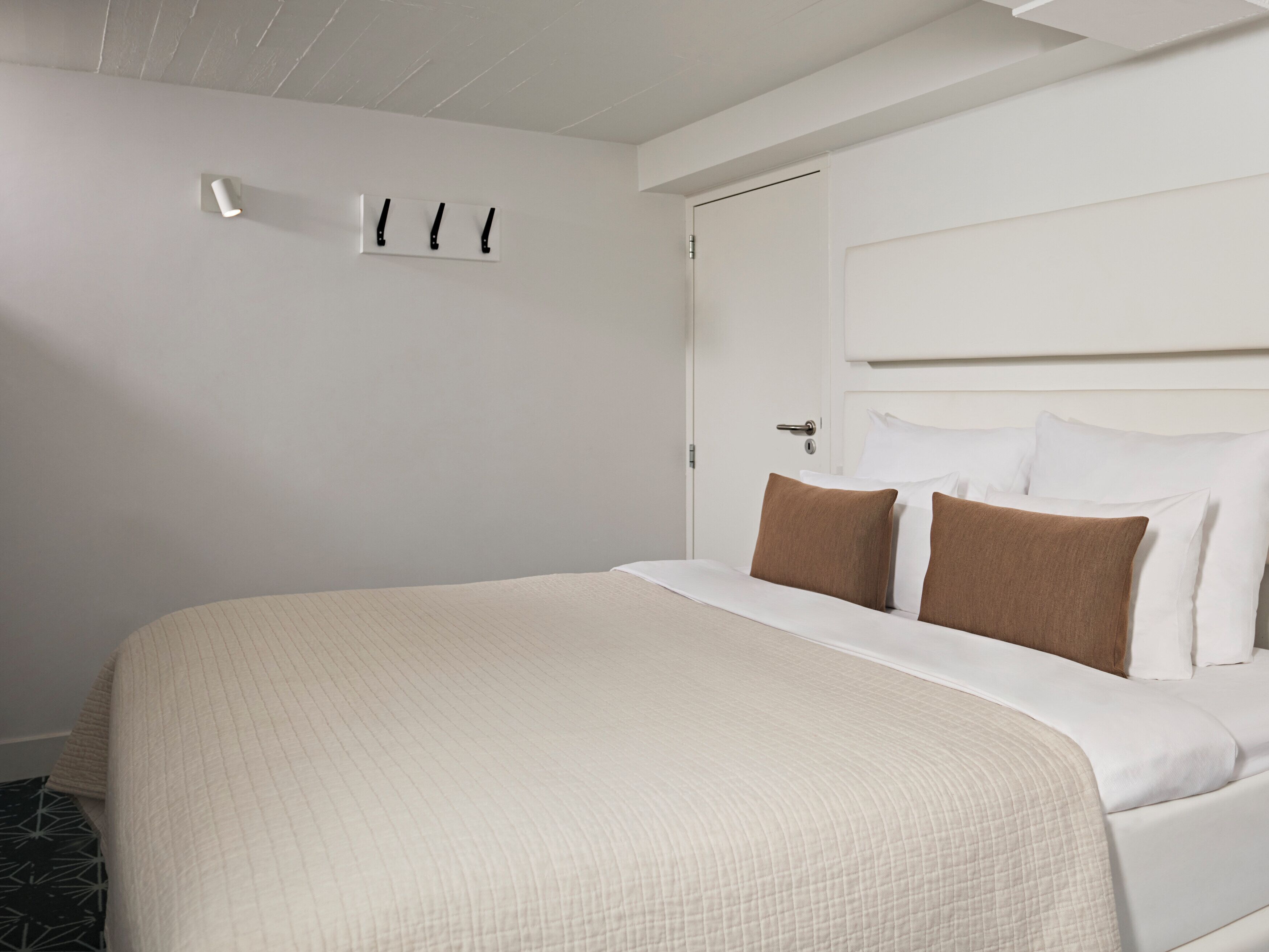 A neatly made bed with a headboard, a bedside table, and a wall-mounted light fixture.
