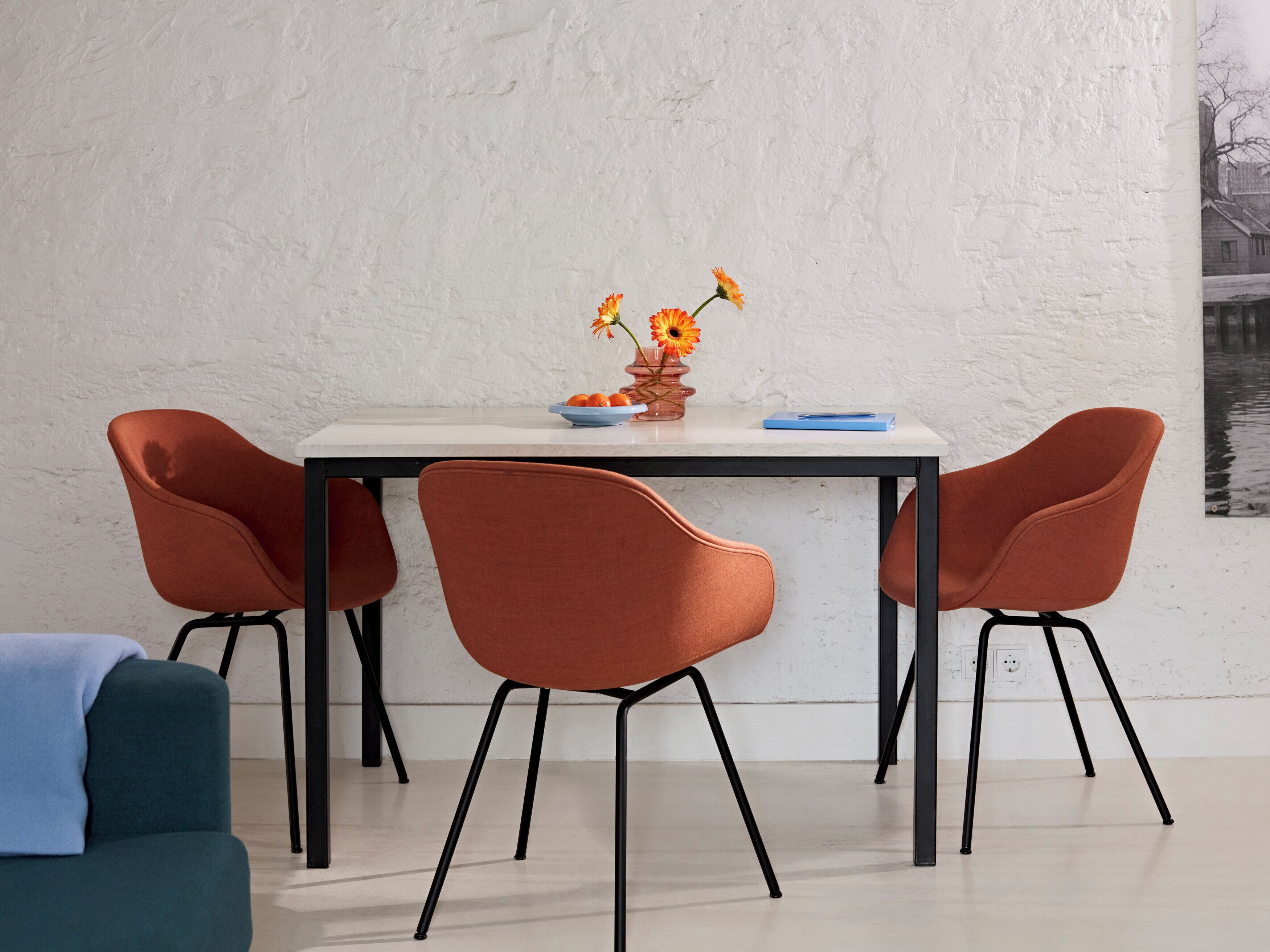 A dining table with four chairs, a vase with flowers, and a blue book on the table.