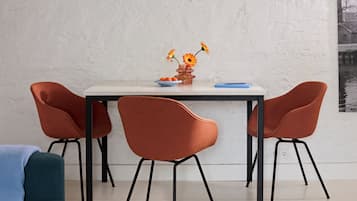 A dining table with four chairs, a vase with flowers, and a blue book on the table.