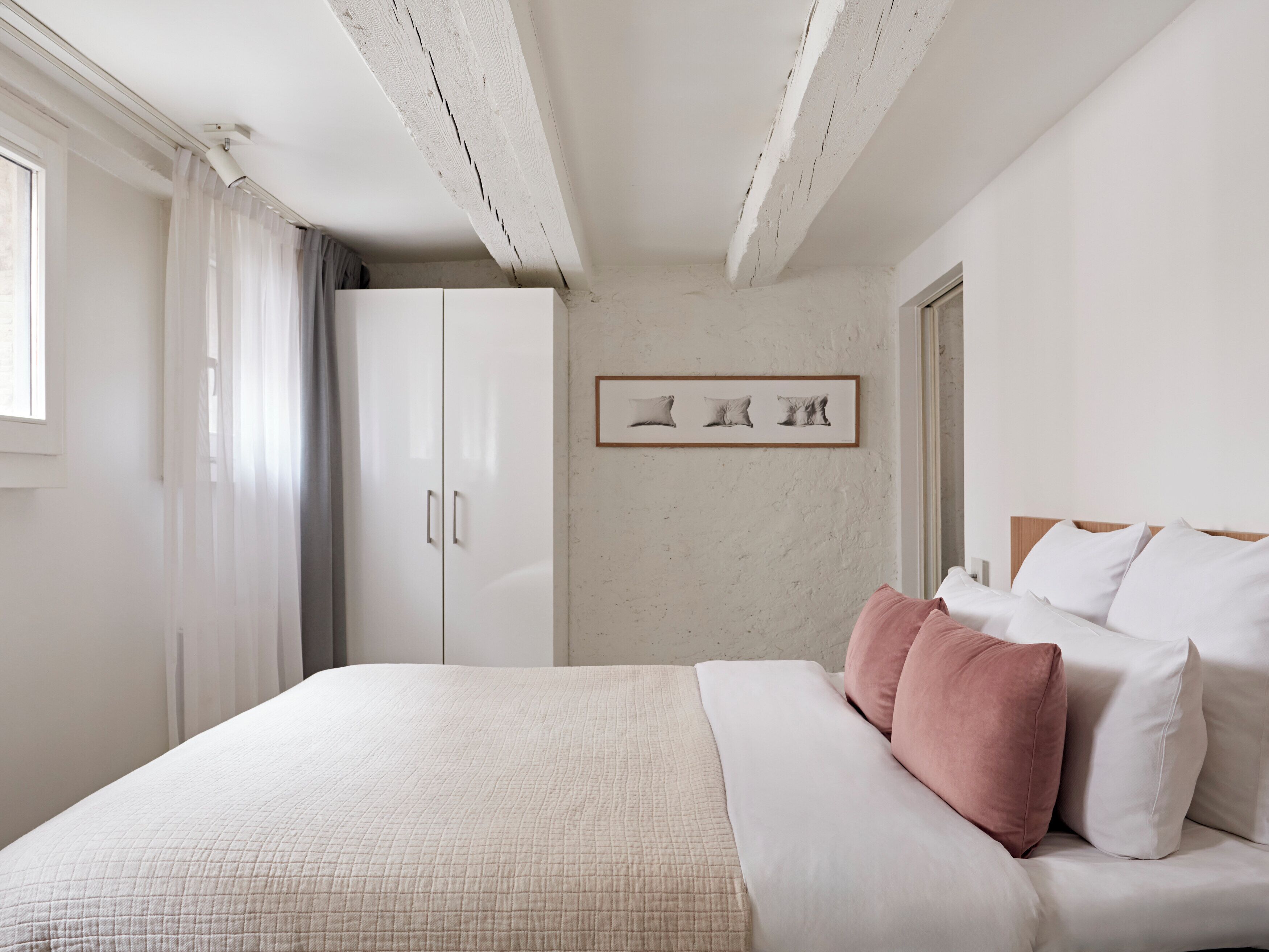 A bedroom with a bed, a wardrobe, a framed picture on the wall, and a window with curtains.