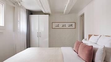 A bedroom with a bed, a wardrobe, a framed picture on the wall, and a window with curtains.