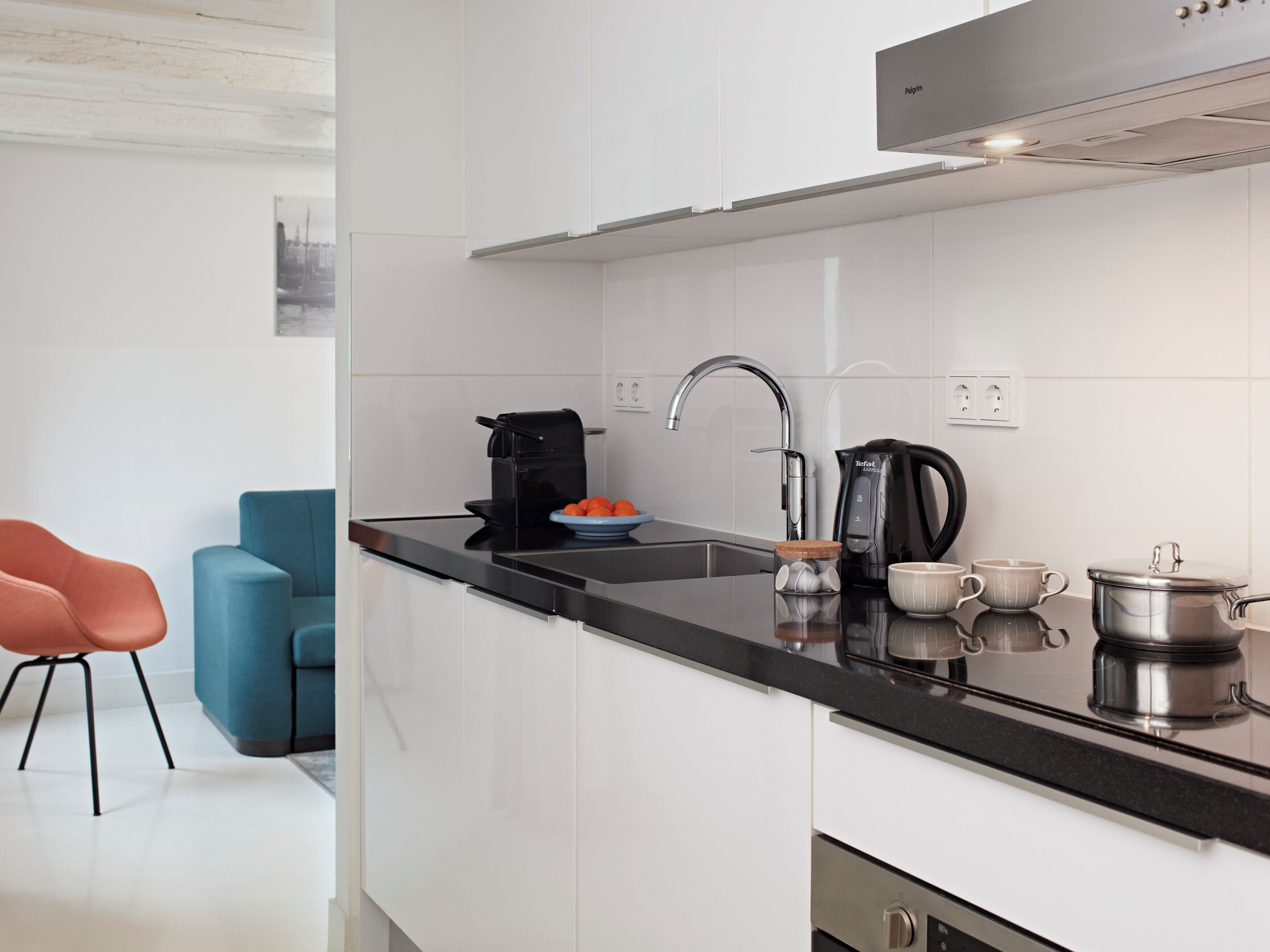 A modern kitchen with white cabinets, a black countertop, a coffee maker, a kettle, and a pot.