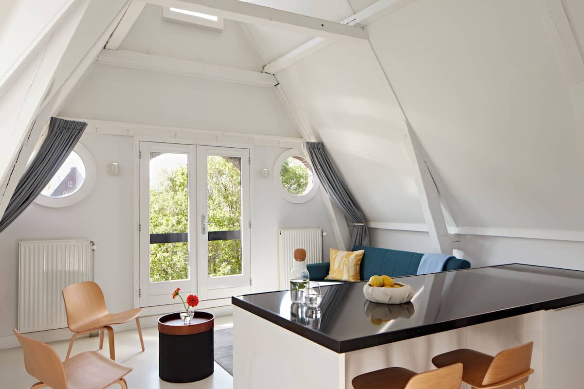 A modern kitchen with a central island, two round windows, and a view of greenery outside.