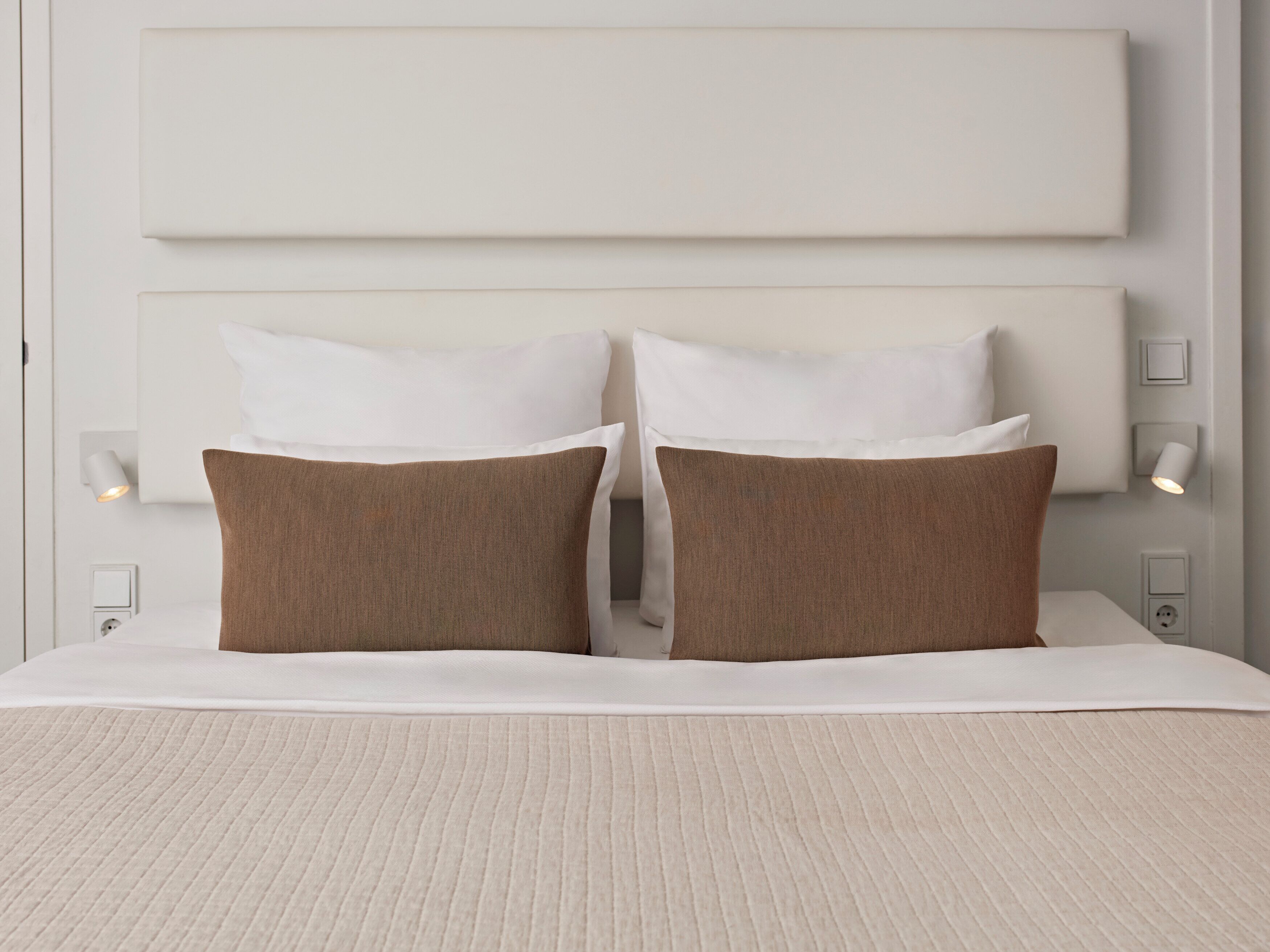Een bed met een wit hoofdbord, twee witte kussens en twee bruine kussens.