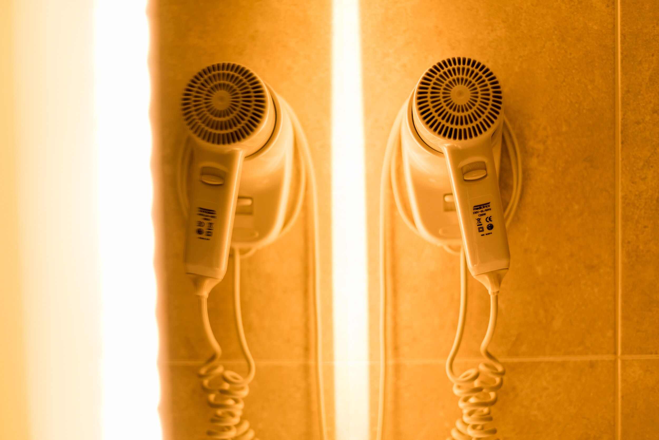Two hair dryers mounted on a tiled wall.