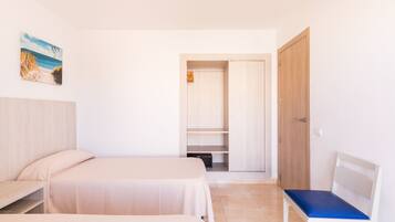 Un dormitorio con dos camas, un banco, un armario y un cuadro de una playa.
