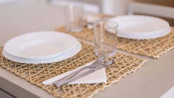 Una mesa de comedor con platos blancos, cubiertos y un vaso sobre un camino de mesa tejido.