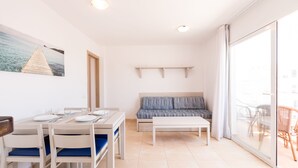 A modern living room with a dining area, a sofa, and a glass door leading to an outdoor seating area. - Apartamentos Avenida - MC Apartamentos Ibiza (Ibiza Town)