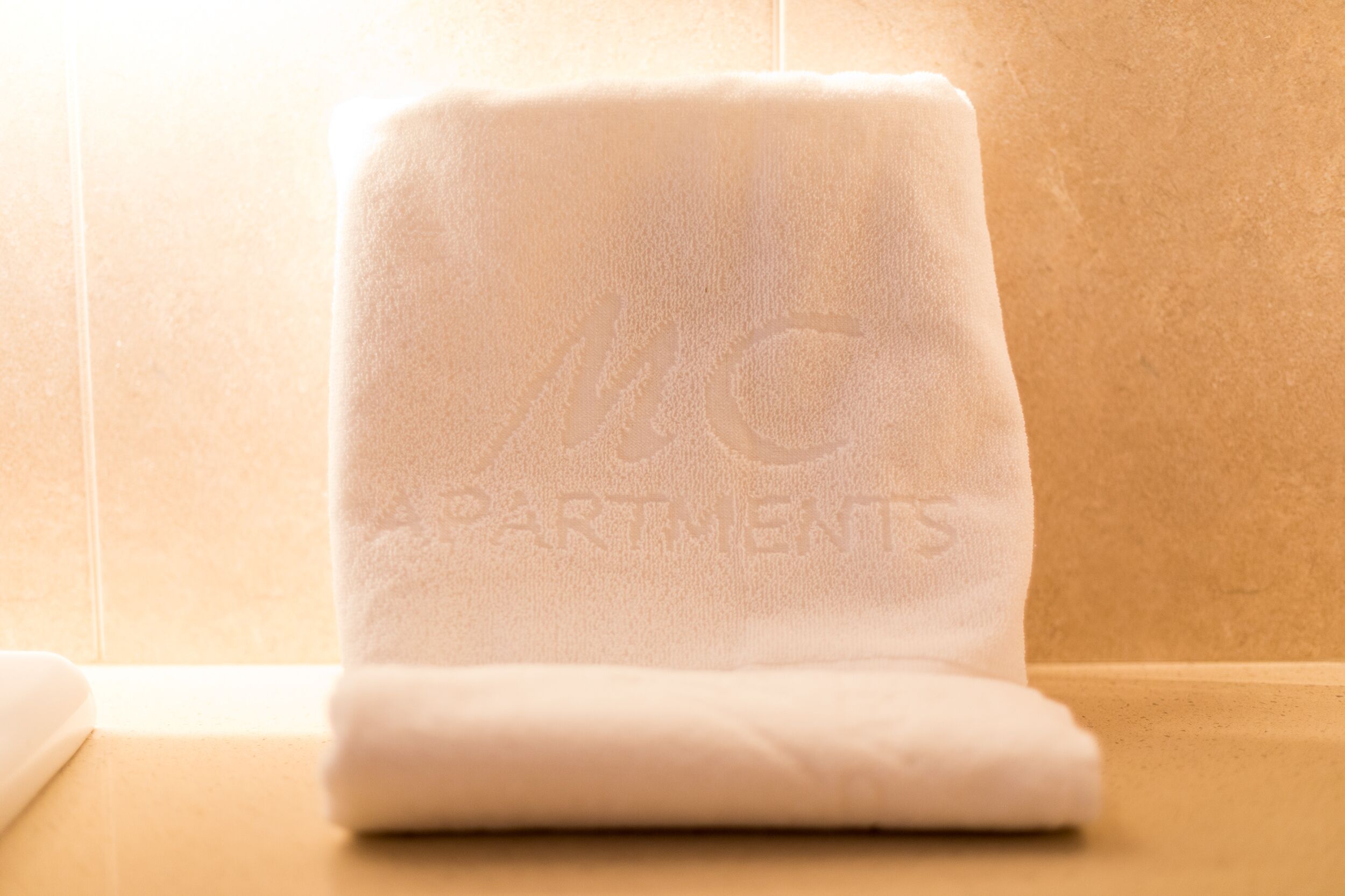 A folded white towel with "APARTMENTS" embossed on it, placed on a beige surface.