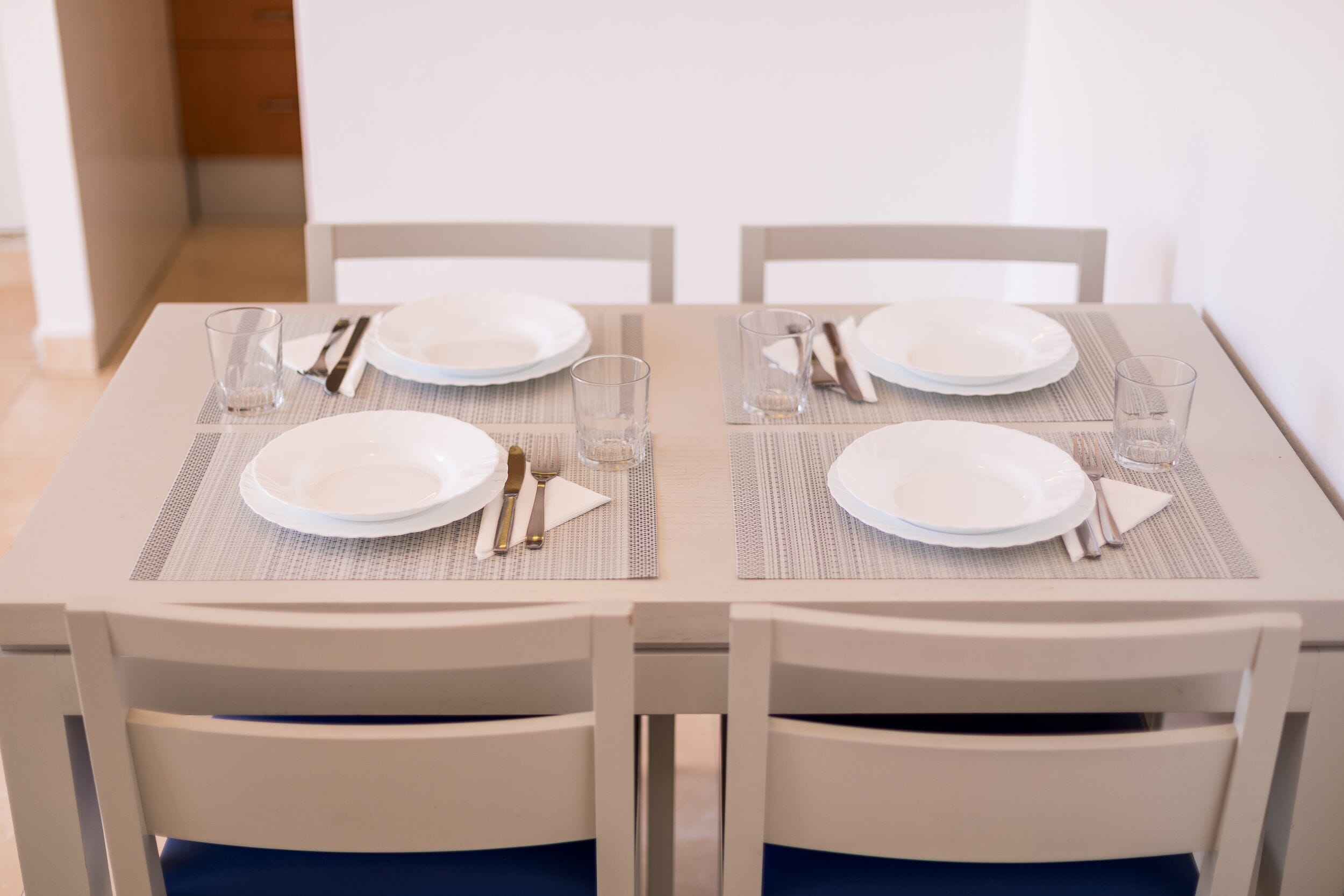 A dining table set with plates, cutlery, and glasses, surrounded by white chairs.