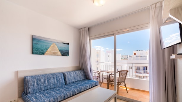 A balcony with a sofa, a table, and a chair. - Apartamentos Avenida - MC Apartamentos Ibiza (Ibiza Town)