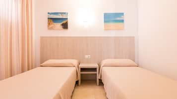 Une chambre avec deux lits, une petite table et deux tableaux sur le thème de la plage accrochés au mur.