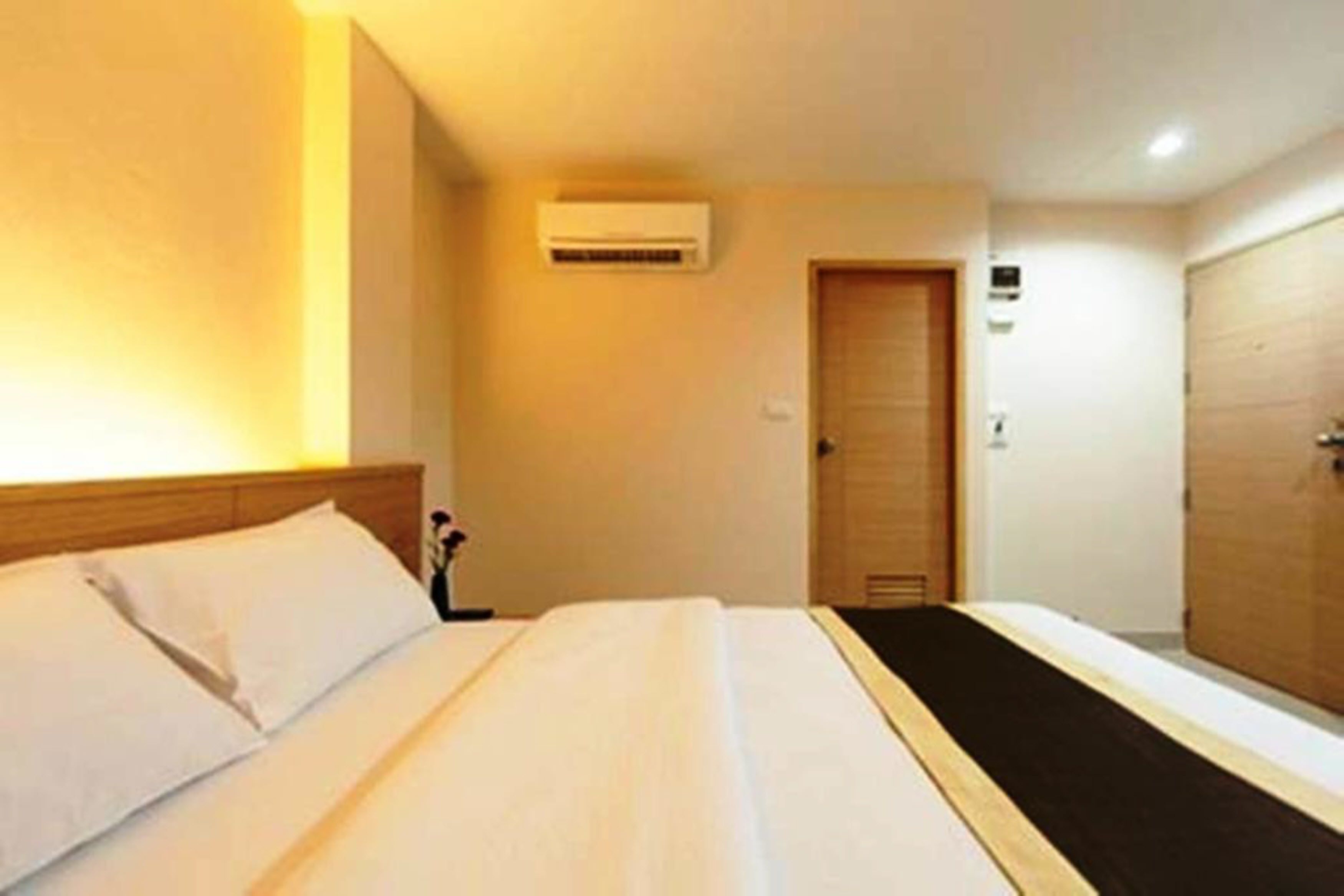 Una habitación de hotel con una cama, un equipo de aire acondicionado, una puerta de madera y un armario.