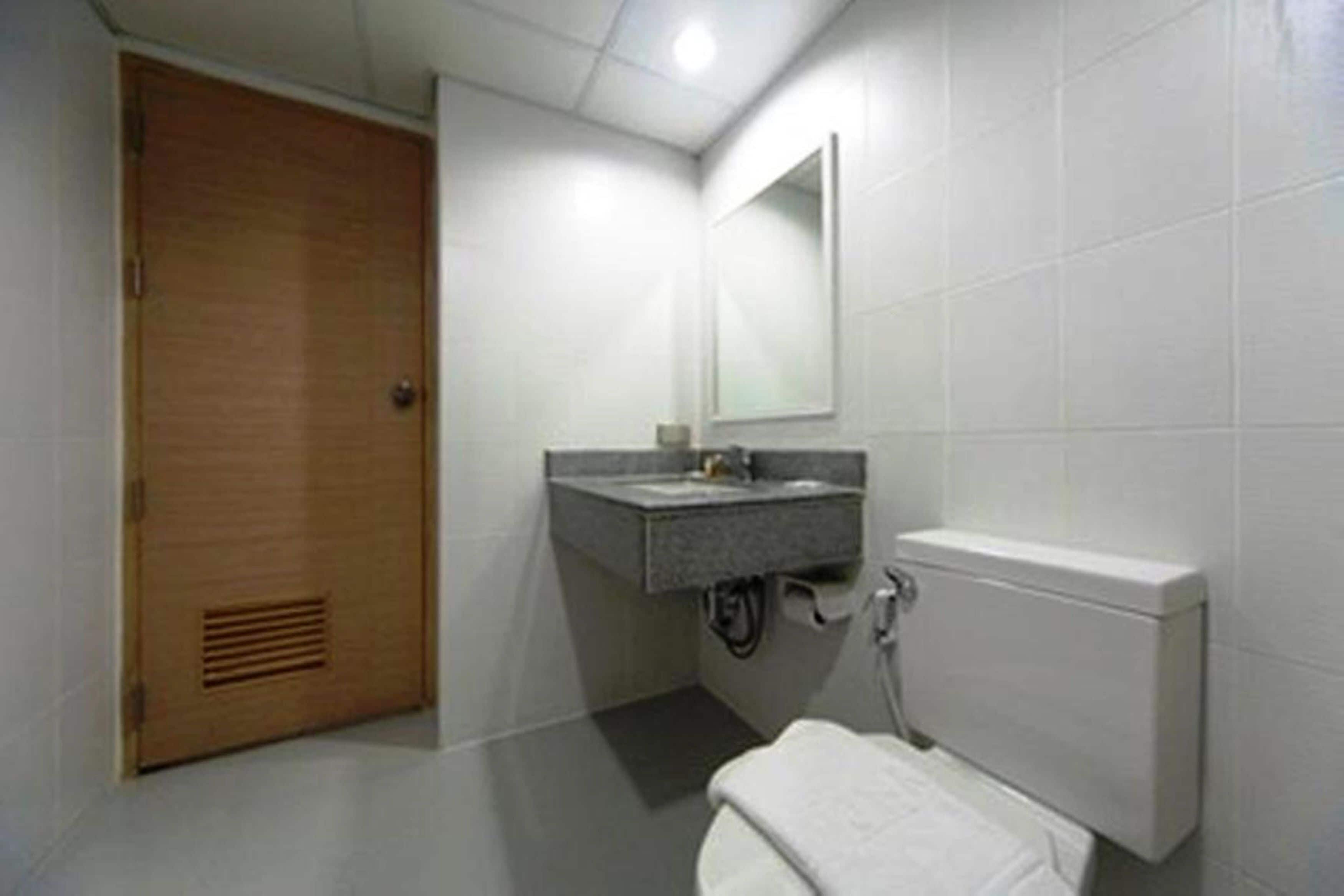 A small bathroom with a wooden door, a sink, a mirror, and a toilet.