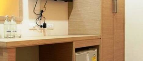 Una habitación de hotel moderna con un escritorio de madera, un televisor montado encima y un refrigerador pequeño debajo.