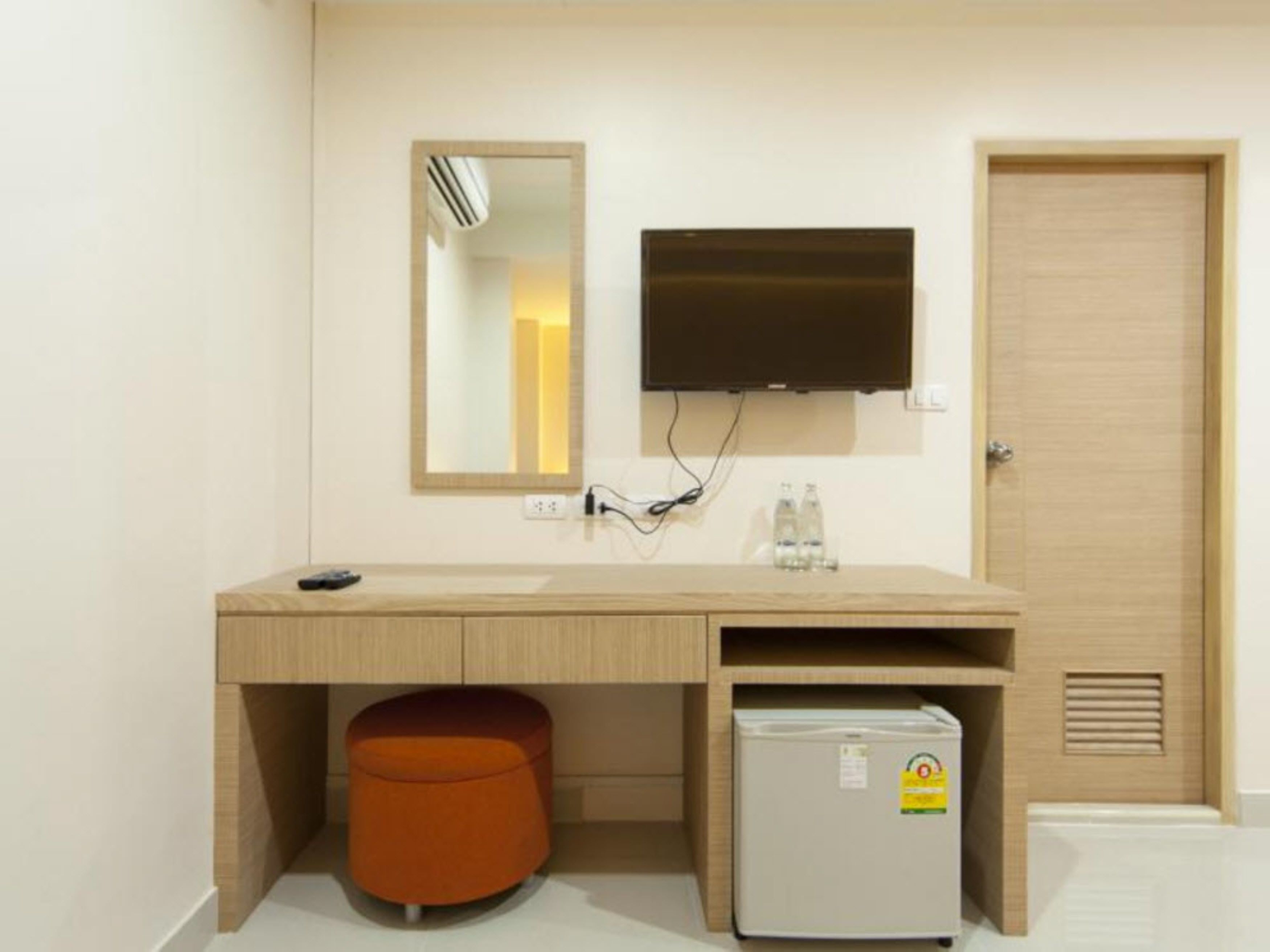 A hotel room with a wooden desk, a mirror, a television, a minibar, and a door.