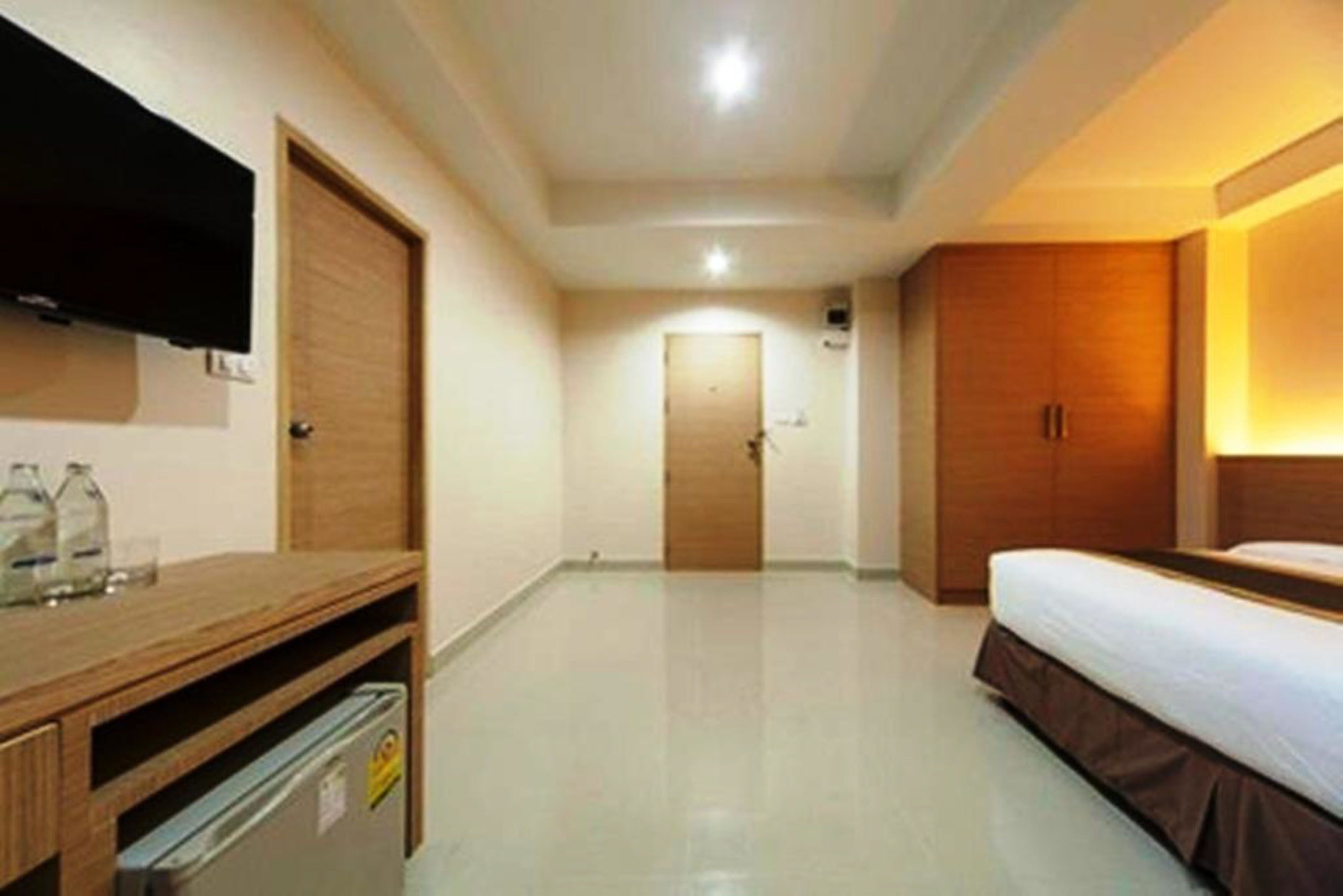 A hotel room with a bed, a wooden dresser, a TV mounted on the wall, and a door in the background.
