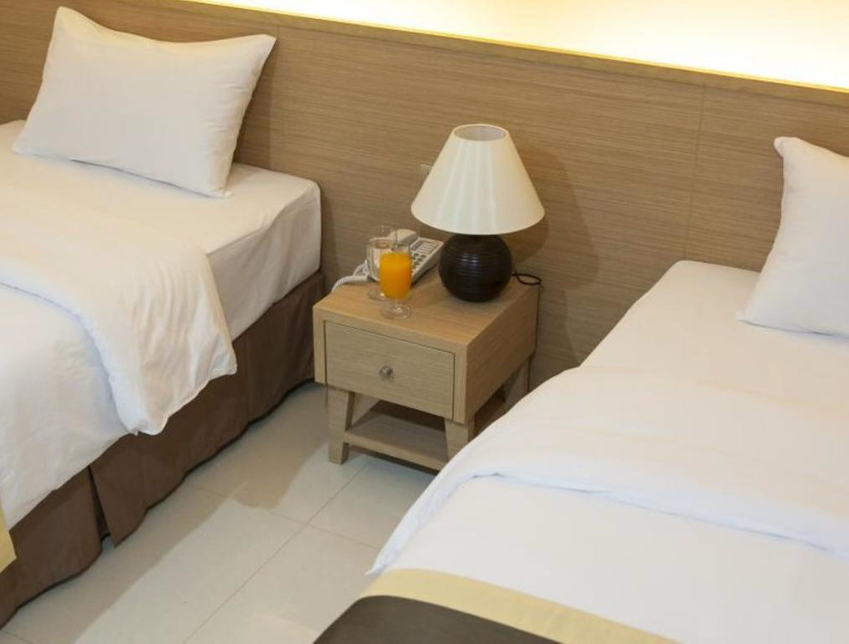Une chambre d’hôtel avec deux lits simples, une table de chevet avec une lampe, un verre de jus d’orange et un téléphone.
