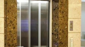 Un ascensor moderno con puerta de cristal y acabado metálico, rodeado por una pared de piedra con vetas.