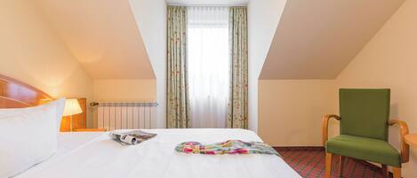 A hotel room with a bed, a chair, a window with curtains, and a radiator.
