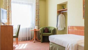 A hotel room with a bed, a chair, a small table with a cup and fruit, a TV, and a window with curtains.