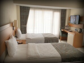 Ein Hotelzimmer mit zwei Betten, einem Schreibtisch, einem Fernseher und einem Fenster mit Vorhängen.