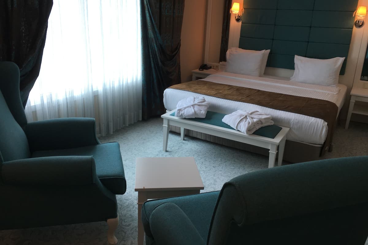 A hotel room with a bed, two chairs, a small table, and a bench.