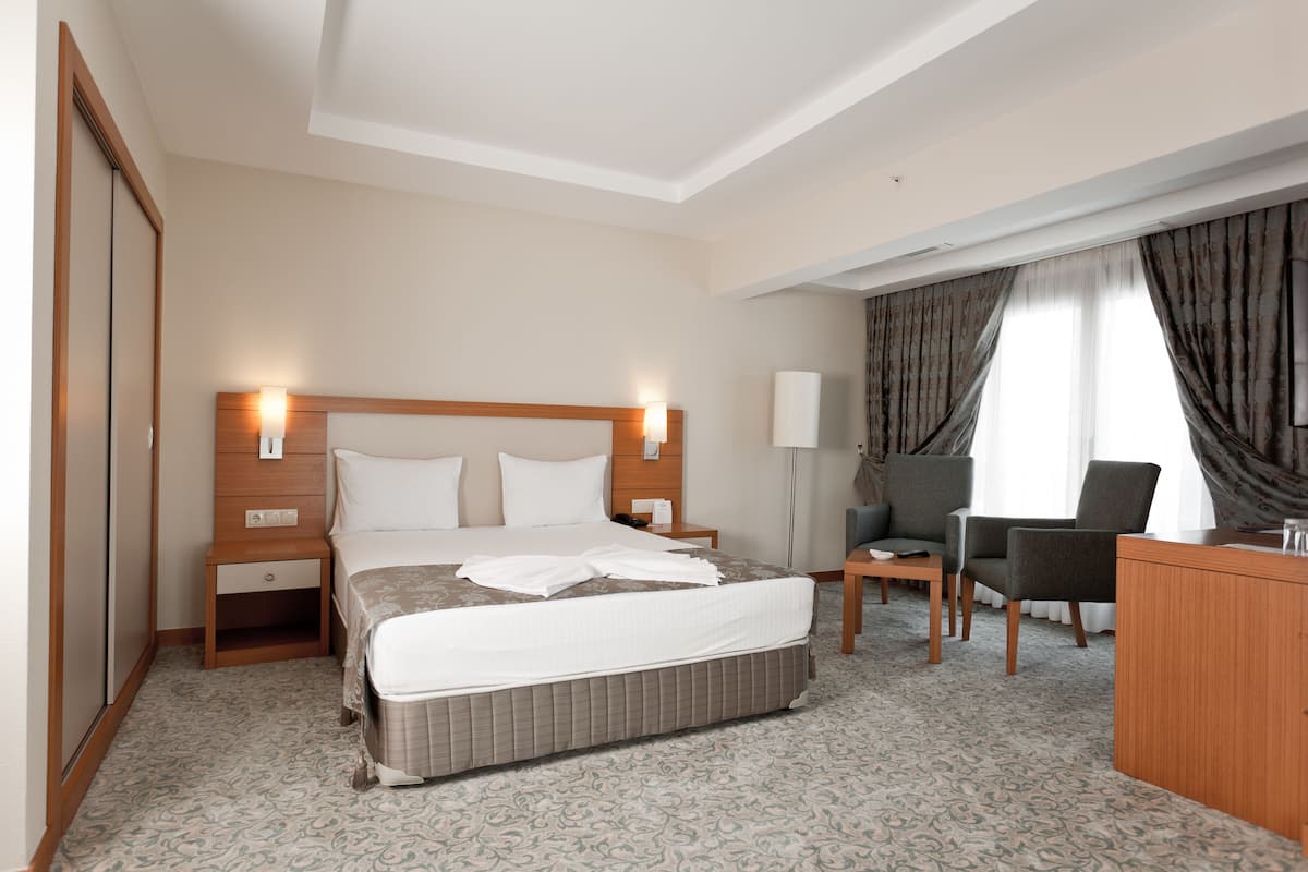 A hotel room with a large bed, bedside tables, a desk, a chair, and a wardrobe.