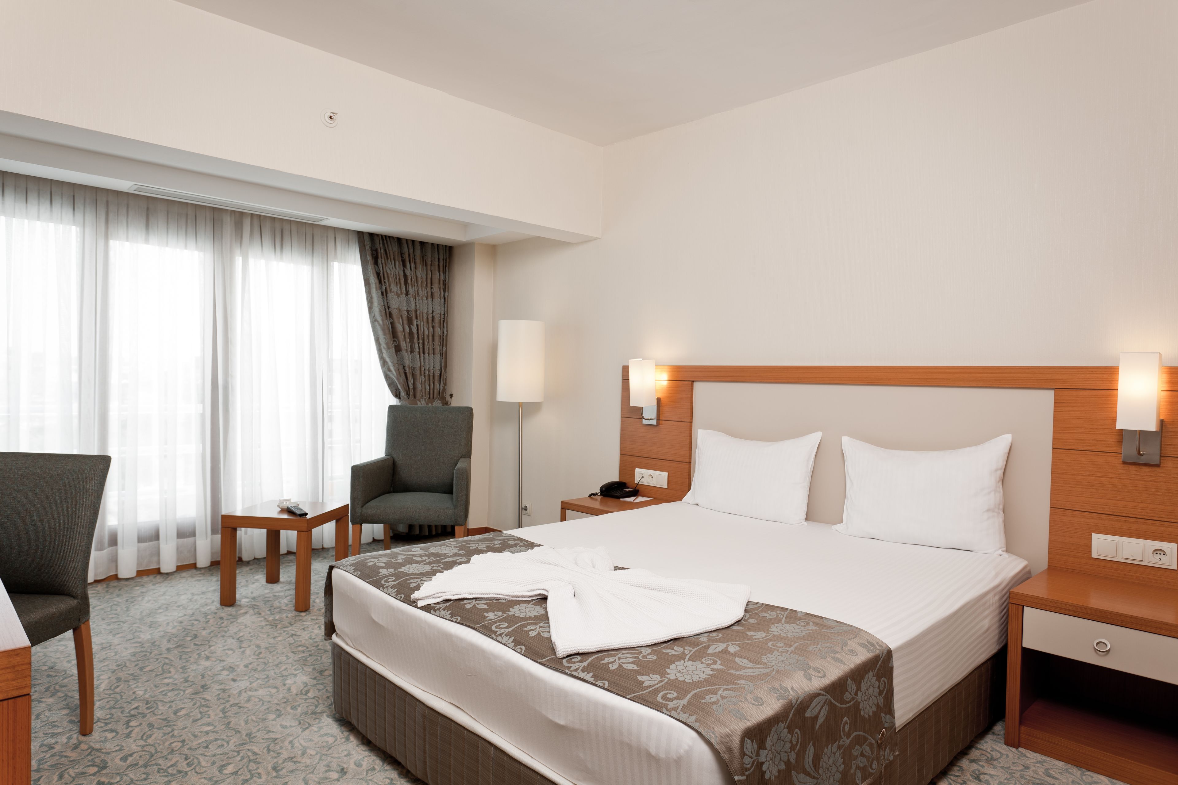 A hotel room with a large bed, a desk, a chair, a lamp, and a window with curtains.