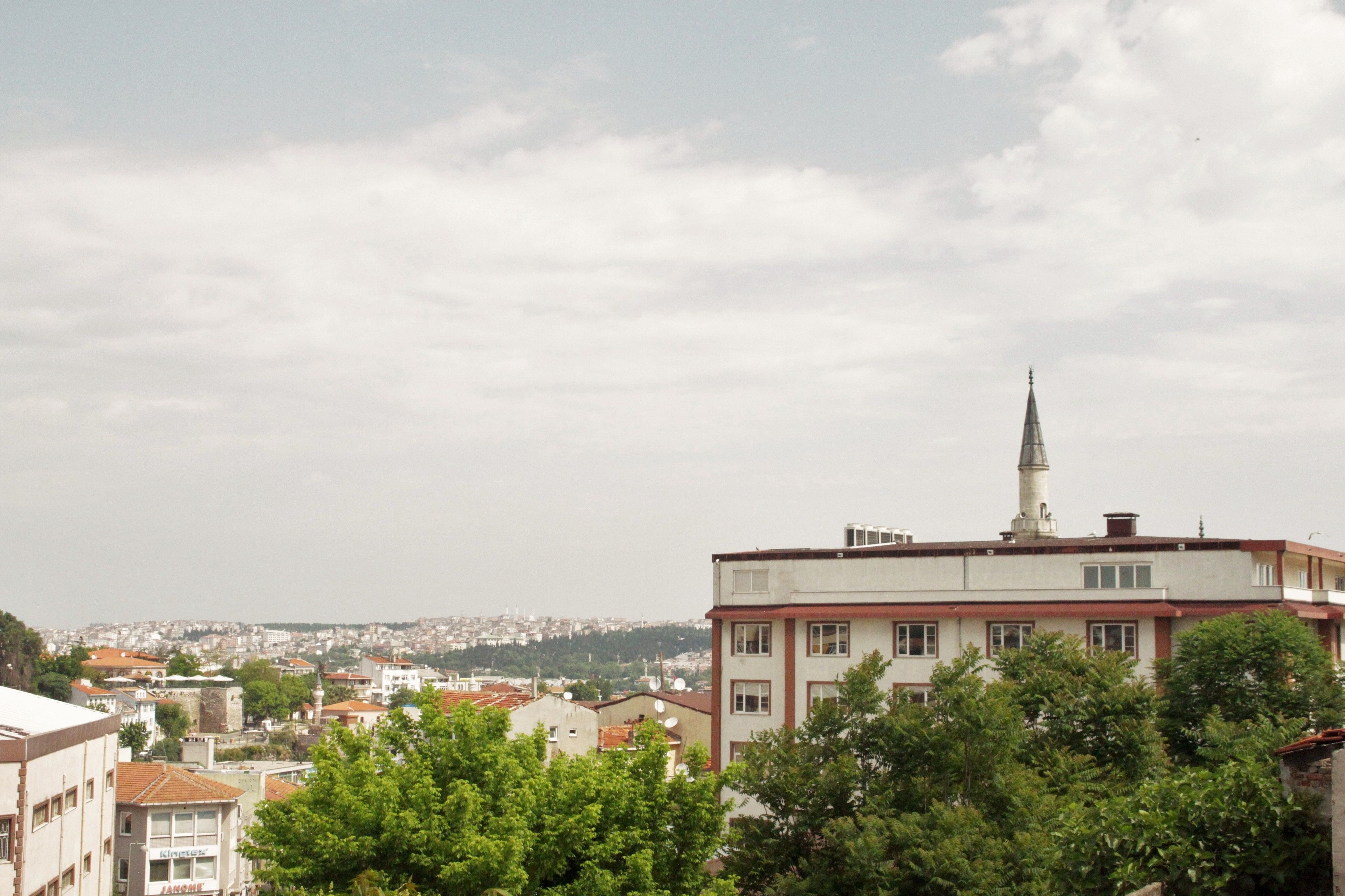 A multi-story building with a prominent tower, surrounded by greenery and other buildings in the background.