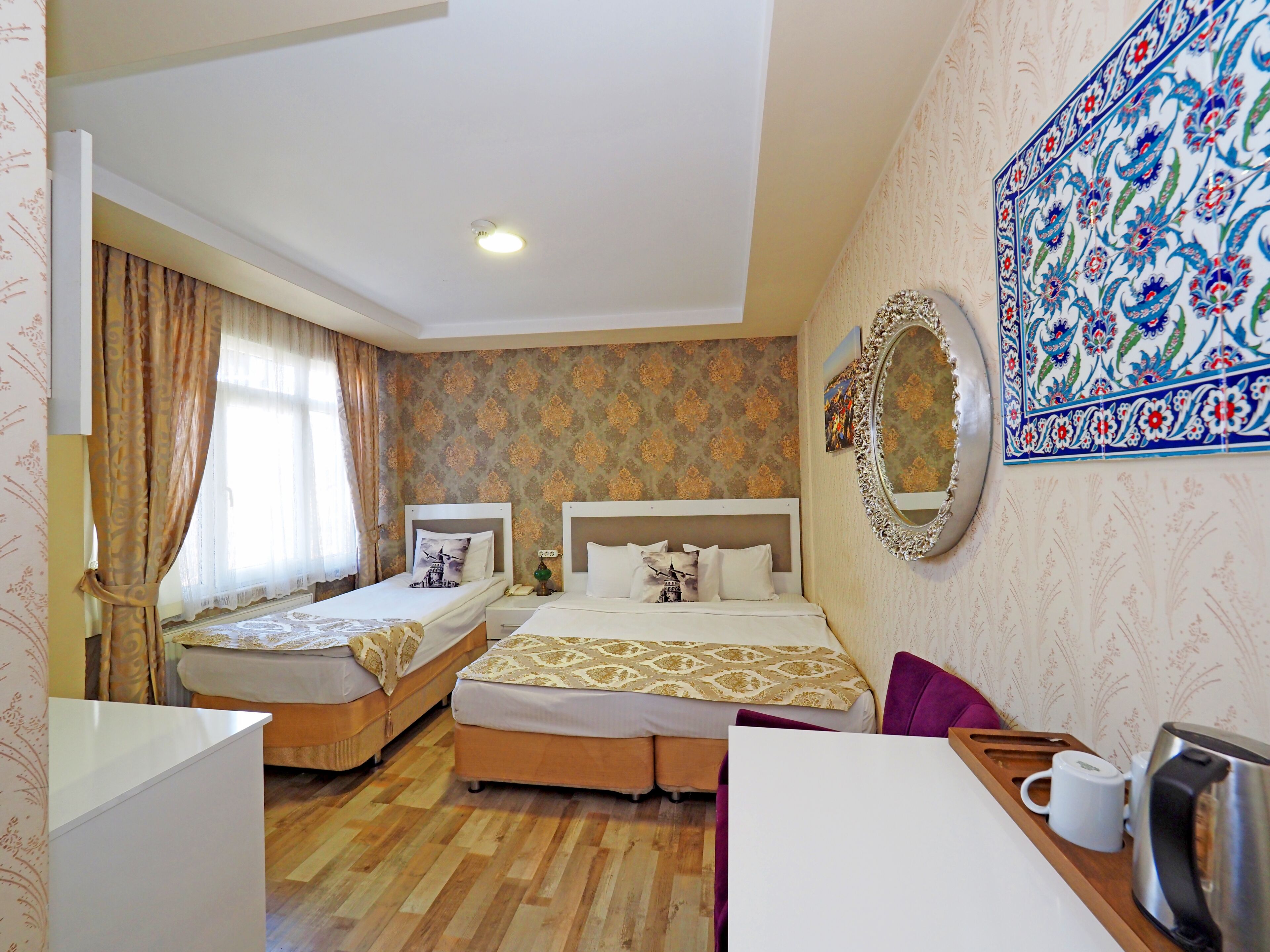A hotel room with two beds, a desk, a chair, a coffee maker, and a decorative mirror.