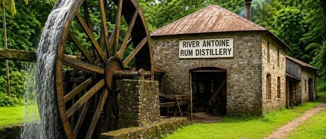 A historic building with a large water wheel and a sign reading 'River Antoine Rum Distillery.'