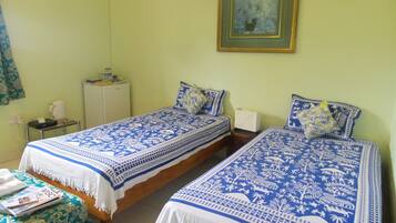 A room with two beds, each with blue and white patterned bedding, a small table with a white lamp, and a painting on the wall.