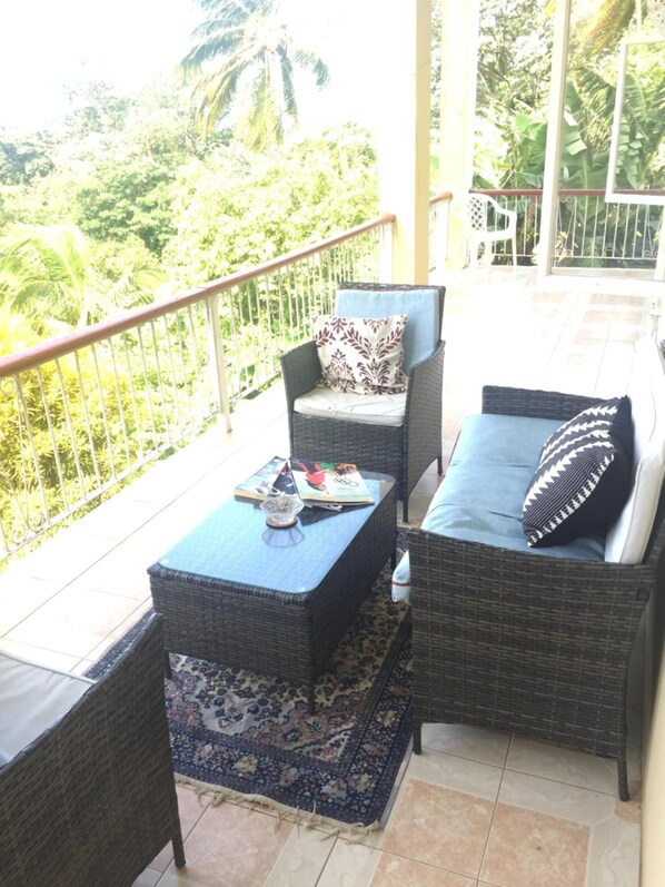 A balcony with wicker furniture, a patterned rug, and a view of greenery. - RNM The Clubhouse Grenada (St. John)