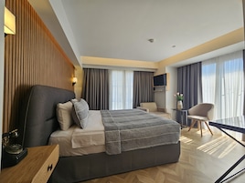 Una habitación de hotel moderna con una cama grande, un escritorio con teléfono, una silla, un televisor montado en la pared y una ventana con cortinas.