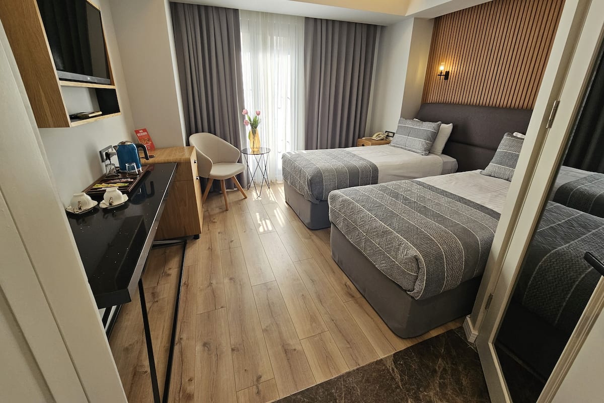 Habitación de hotel con dos camas, un escritorio con silla, una mesita con un florero y un panel de pared de madera.