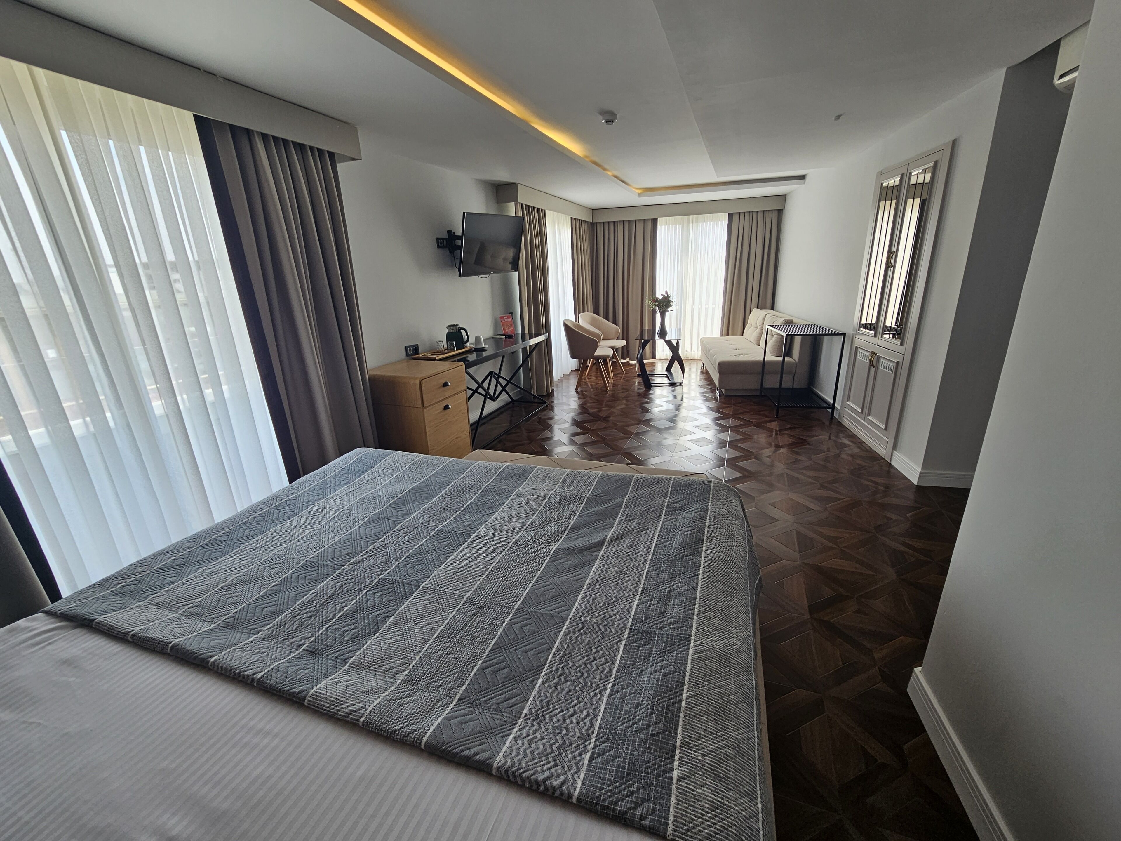Une chambre d’hôtel avec un grand lit, un bureau avec une chaise, un canapé et un téléviseur fixé au mur.