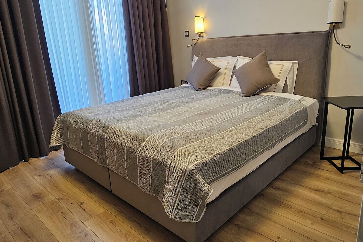 Una cama bien hecha con una colcha estampada, un cabecero con dos almohadas, una mesita de noche y una lámpara de pared.