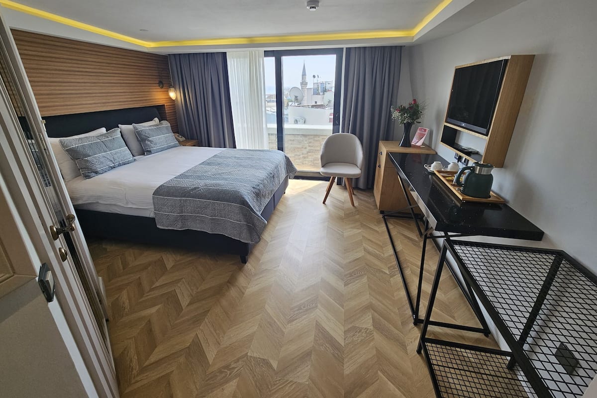Una habitación de hotel con cama, escritorio, silla, televisor y vista a la ciudad.
