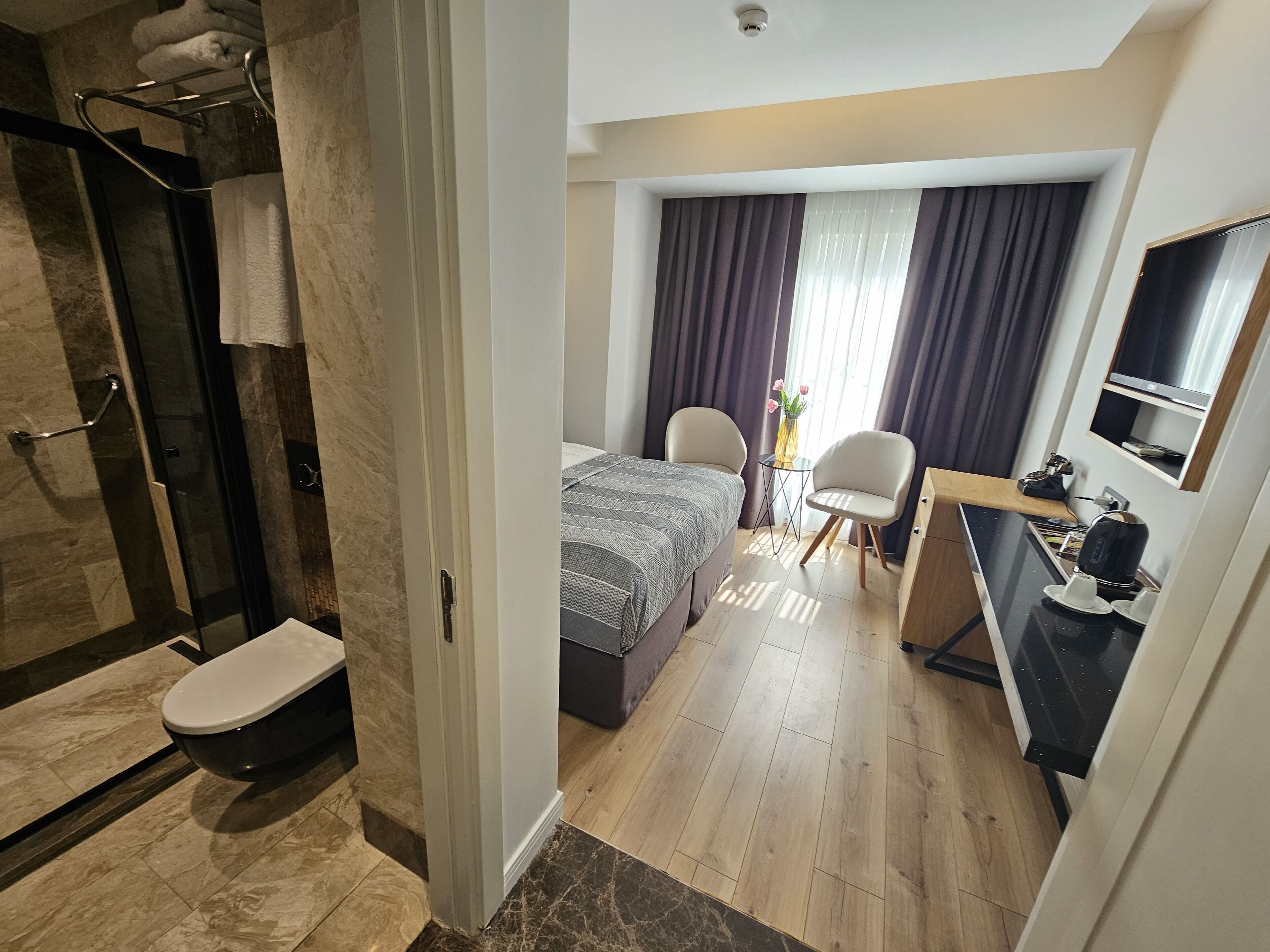 A modern hotel room with a shower, toilet, bed, and a small kitchenette.