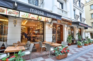 An outdoor seating area with wicker chairs and tables, a bistro named 'massa bistro' with a menu display, and a hotel entrance named 'Aventis Hotel'.