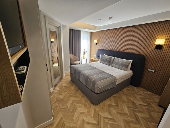 A modern hotel room with a large bed, wooden panel wall, and a small desk with a lamp. - Anthemis Hotel (Istanbul)