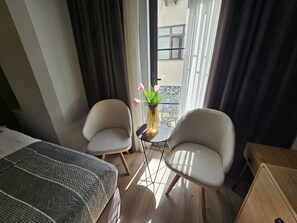 A hotel room with a bed, two armchairs, a small table with a vase of flowers, and a balcony with a railing. - Anthemis Hotel (Istanbul)