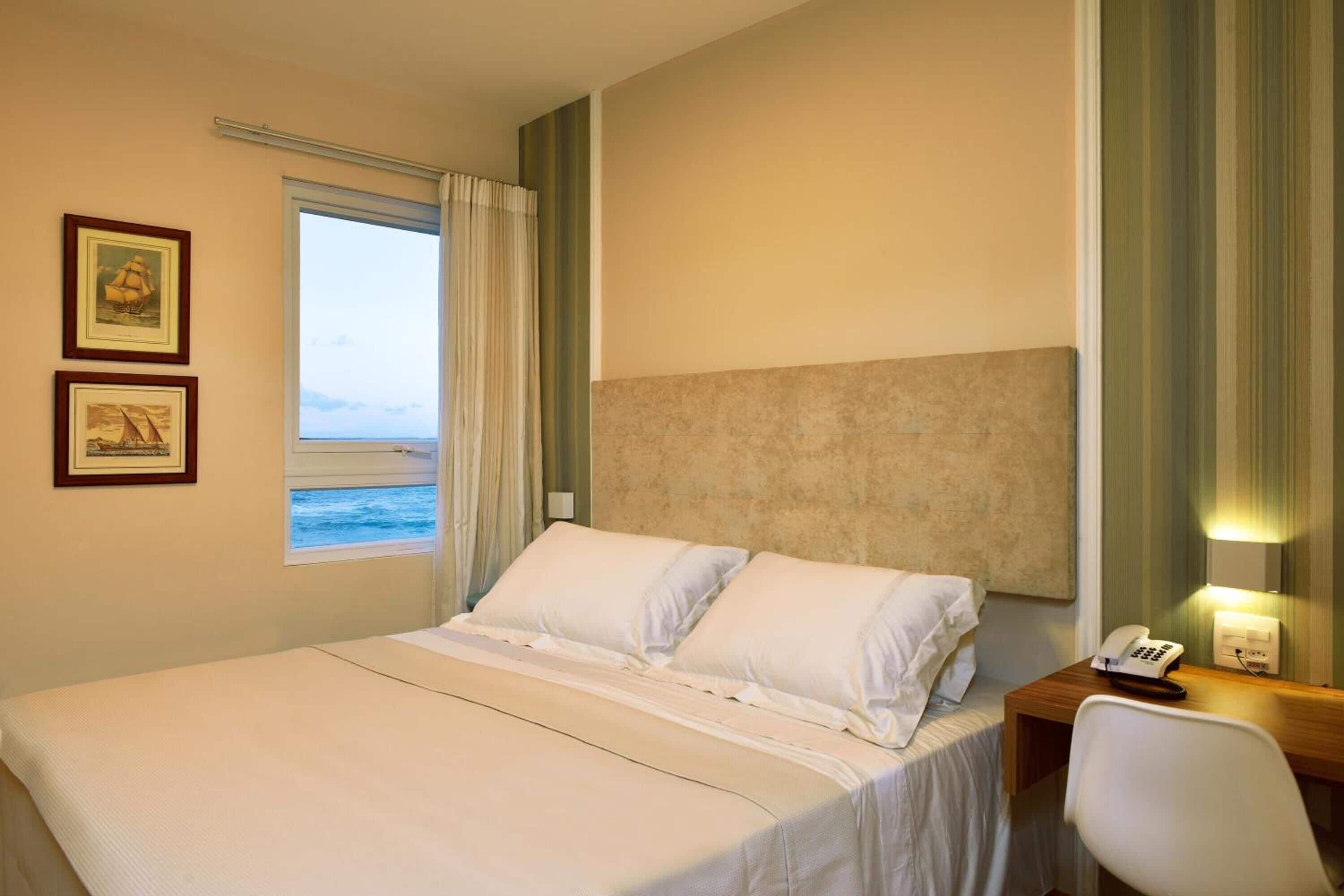 A hotel room with a bed, a desk with a telephone, and a window with curtains.