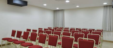 A conference room with rows of red chairs and a white ceiling with recessed lighting.