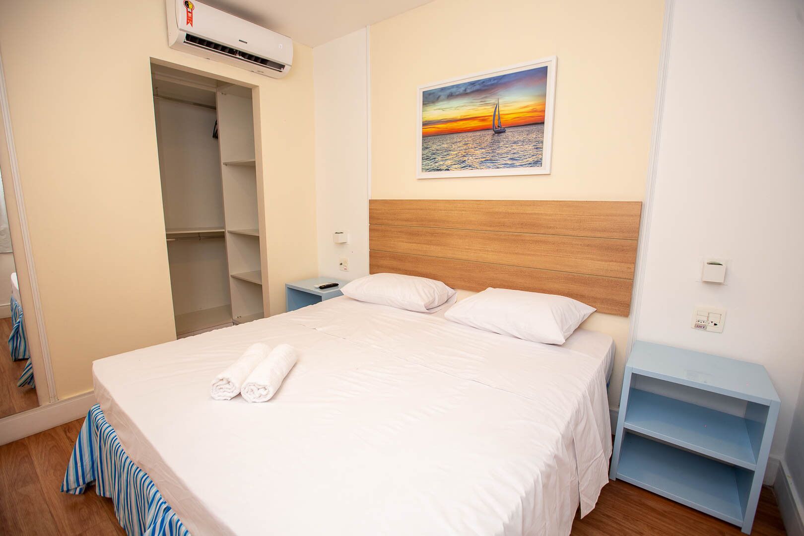 A hotel room with a bed, a nightstand, a wardrobe, and a painting of a sunset over the ocean.