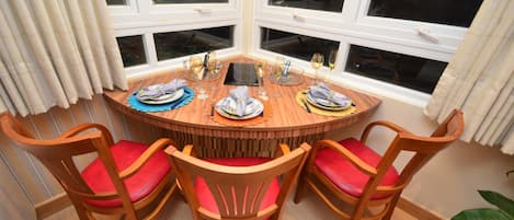 Una mesa redonda de madera con cuatro sillas, cada una con un cojín rojo. La mesa está dispuesta para una comida con platos, vasos y cubiertos.
